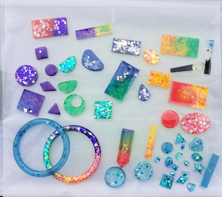a photo of an assortment of cast epoxy resin jewelry pieces. Most of them have glitter inclusions.