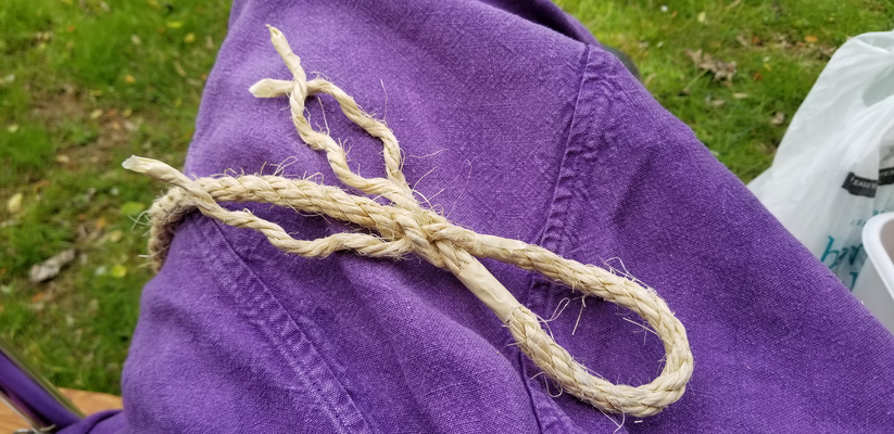 a photo of a partially-worked three-strand eye splice in the end of a length of half-inch rope laying 
		across purple linen. There's some very green grass behind the linen.