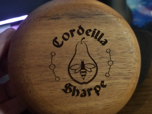 a photograph of the bottom of a wooden bowl. The bowl's bottom has been laser-engraved with a custom design: 
		the bowl owner's name arching over and under a central design of a honeybee within the outline of a pear.