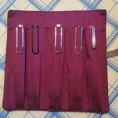 a photo of a pen roll made of dark purple dupioni silk. Five pens are stowed in the pen slots.