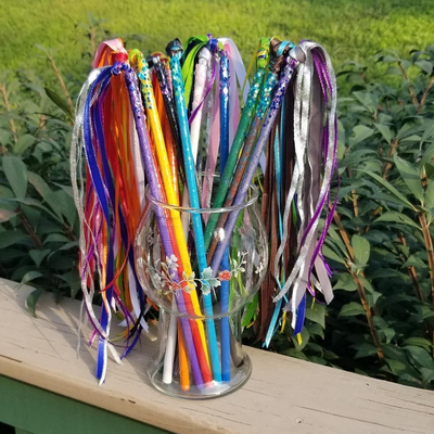 a photo of an assortment of ribbon wands in a glass vase. Each wand is painted a different color and has 
		chunky glitter glued to the ribbon end. A thin coating of epoxy resin over each wand keeps the glitter from traveling. Each wand has a plume of 
		ribbons in coordinating colors attached to an eye screw set into the 'ribbon' end of each wand.