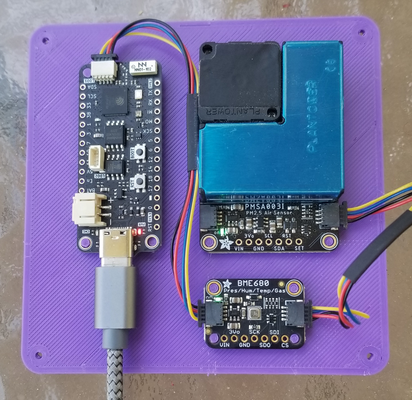 a 3D-printed plate (purple) with three microelectronic components mounted to it. On the left is a 
		Feather S3 controller board. On the top right is a PMSA003i air quality sensor board. On the bottom right is a BME680 temperature/humidity/pressure
		sensor. All three components are wired together. The Feather S3 has a USB-C power cord plugged into it.