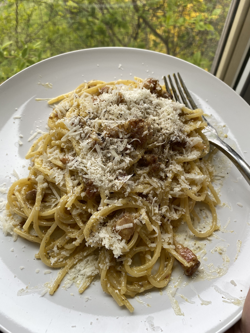 a big plate of carbonara featuring spaghetti coated in a silky egg yolk sauce topped with a good amount of bacon, lots of black pepper, and lots of parmesan cheese.